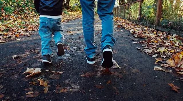 Dospělý a dítě kráčejí vedle sebe po lesní cestě.