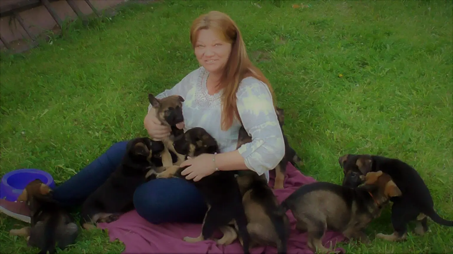 Žena sedí na dece v zahradě mezi malými psy.