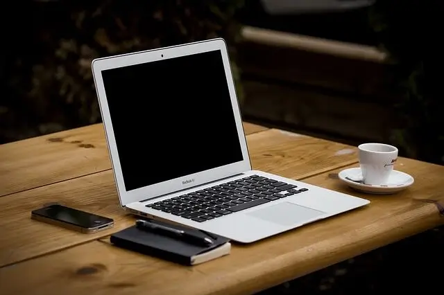 Notebook, telefon a šálek na dřevěném stole.